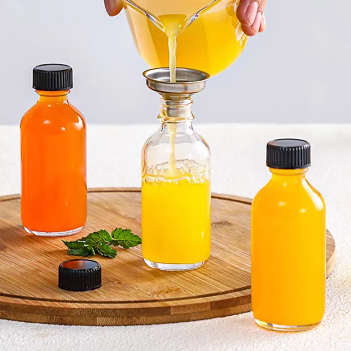 Small glass bottle being filled with yellow beverage on a wooden tray
