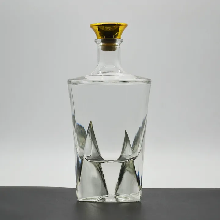 Botella de licor transparente con tapón dorado y cuerpo con relieves geométricos