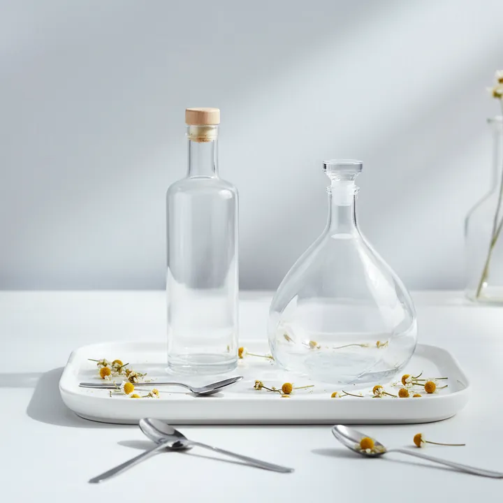 Two clear liquor bottles displayed on a white tray with flowers and metal spoon