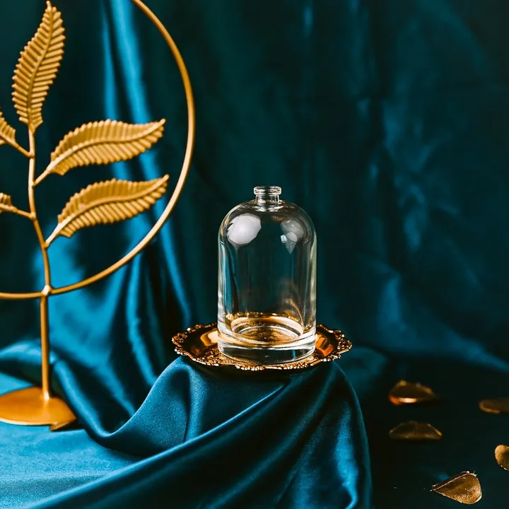 Frasco de perfume transparente con forma de cúpula, presentado sobre terciopelo azul y con adornos dorados
