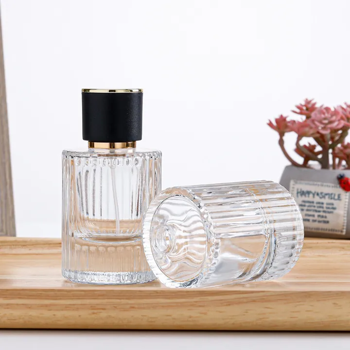 Dos frascos de perfume cilíndricos acanalados con tapones negros y dorados