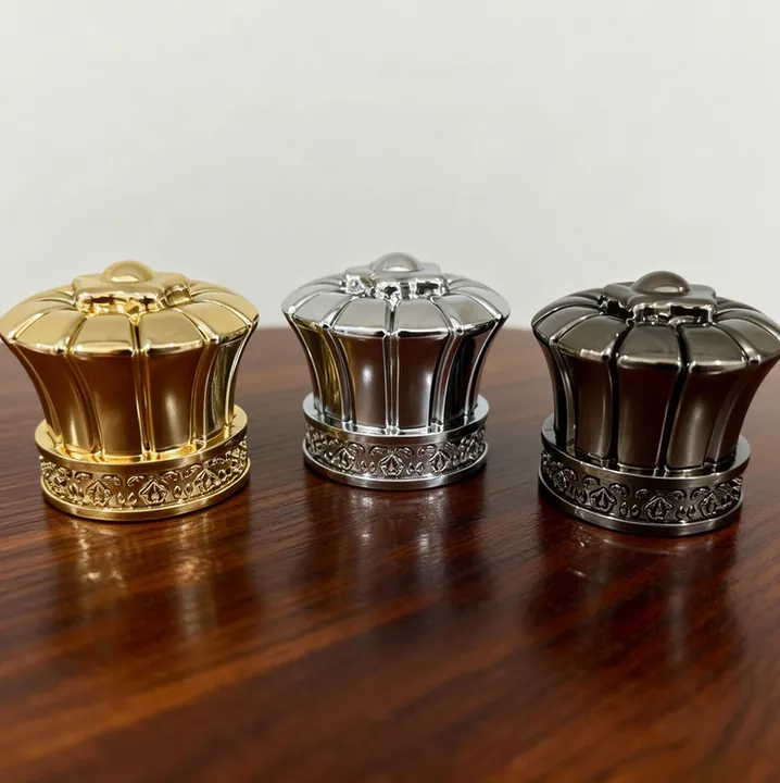 Three crown shaped perfume bottle caps in gold silver and dark colors