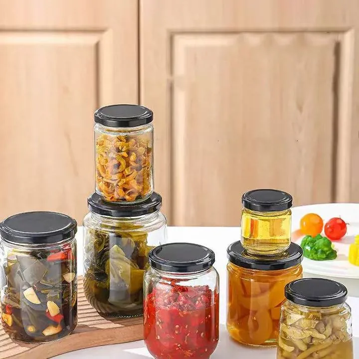 Стеклянные банки для маринованных овощей с чёрными крышками, наполненные соусом чили, маринованными овощами, мёдом и сухими продуктами