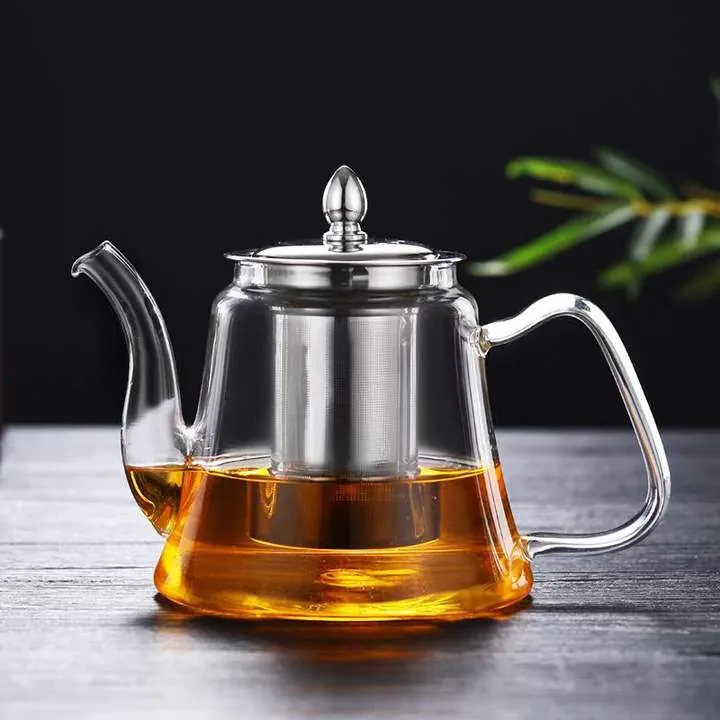 Théière en verre avec infuseur en acier inoxydable posée sur une table sombre