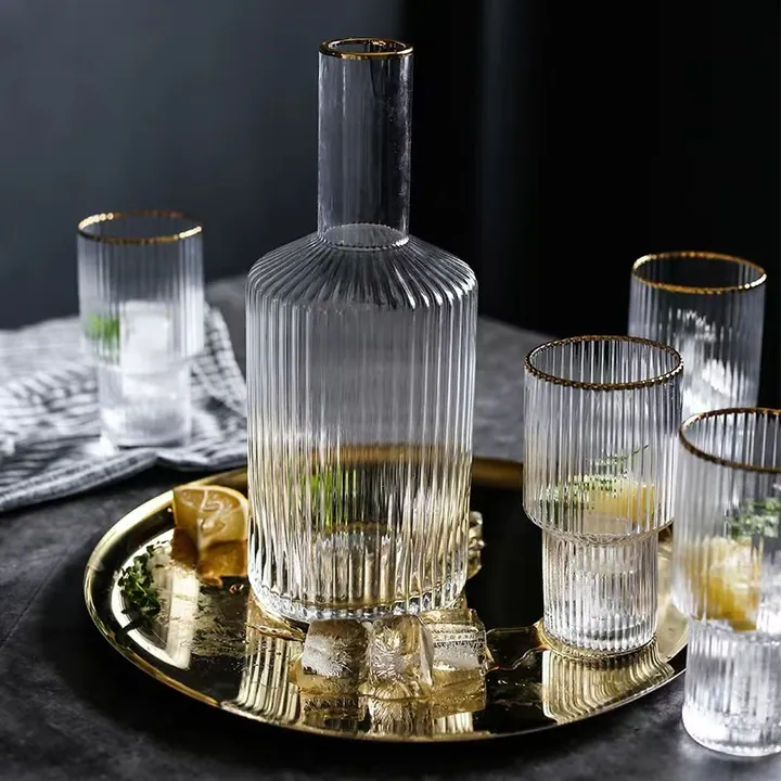 Eine Karaffe aus geripptem Glas und dazu passende Gläser mit goldenem Rand, präsentiert auf einem goldenen Tablett