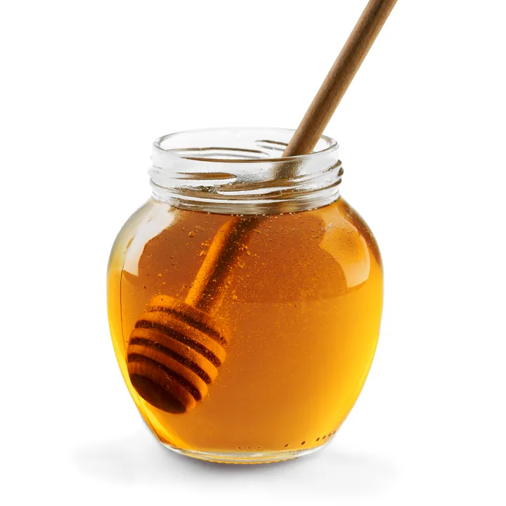 Round clear honey jar filled with honey and paired with a wooden honey dipper