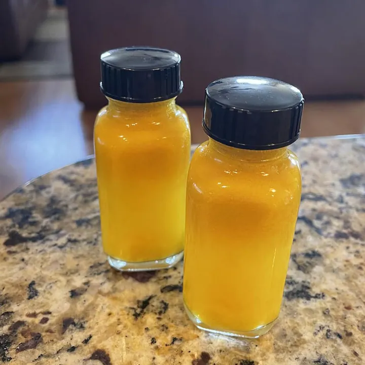 Two round glass shot bottles filled with yellow beverage