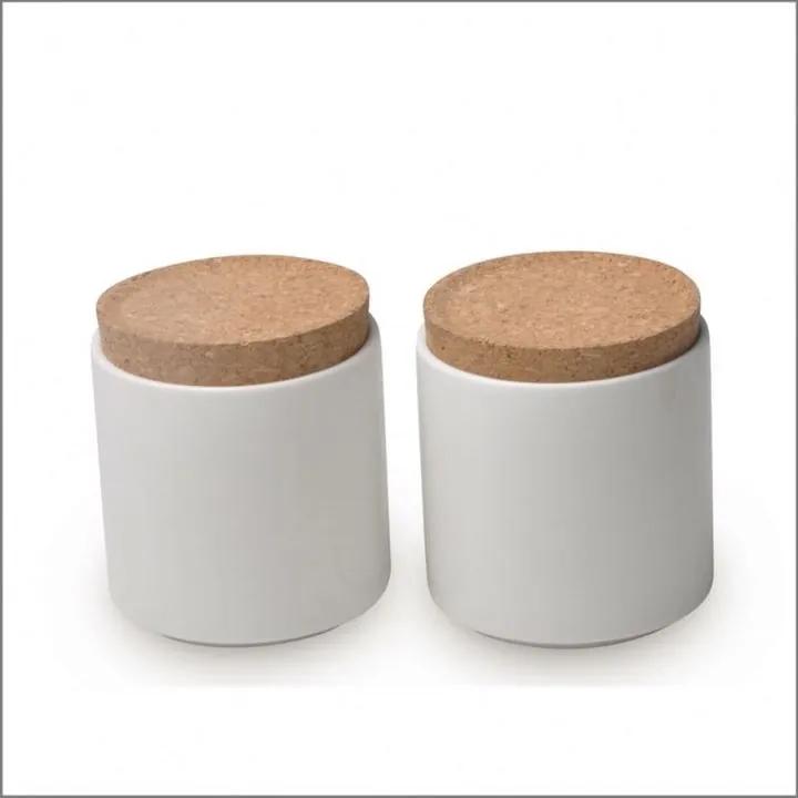 Two white cylindrical candle jars with cork lids