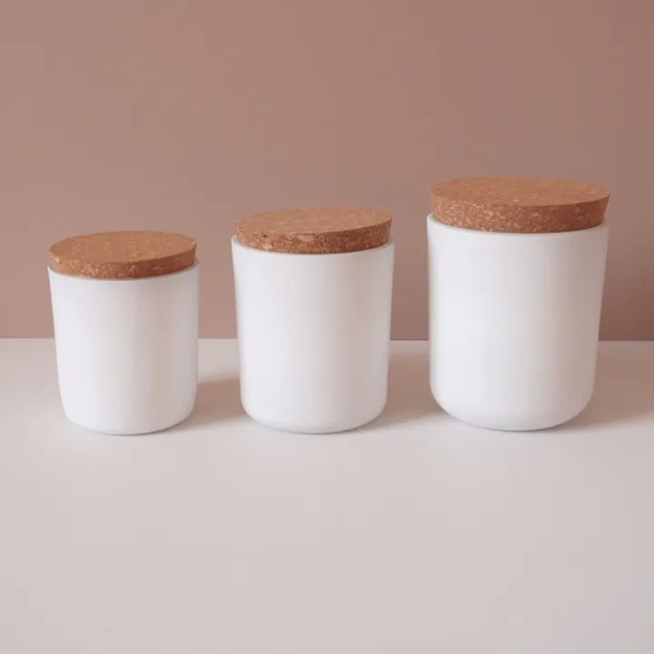 Three white cylindrical candle jars in different sizes with cork lids