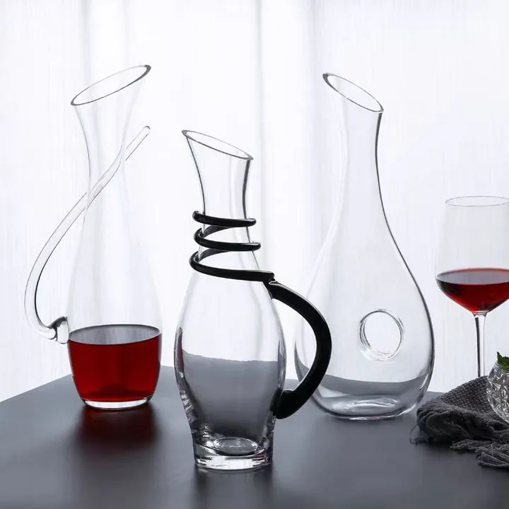 Tres diseños diferentes de decantadores de vino de cristal expuestos junto a copas de vino