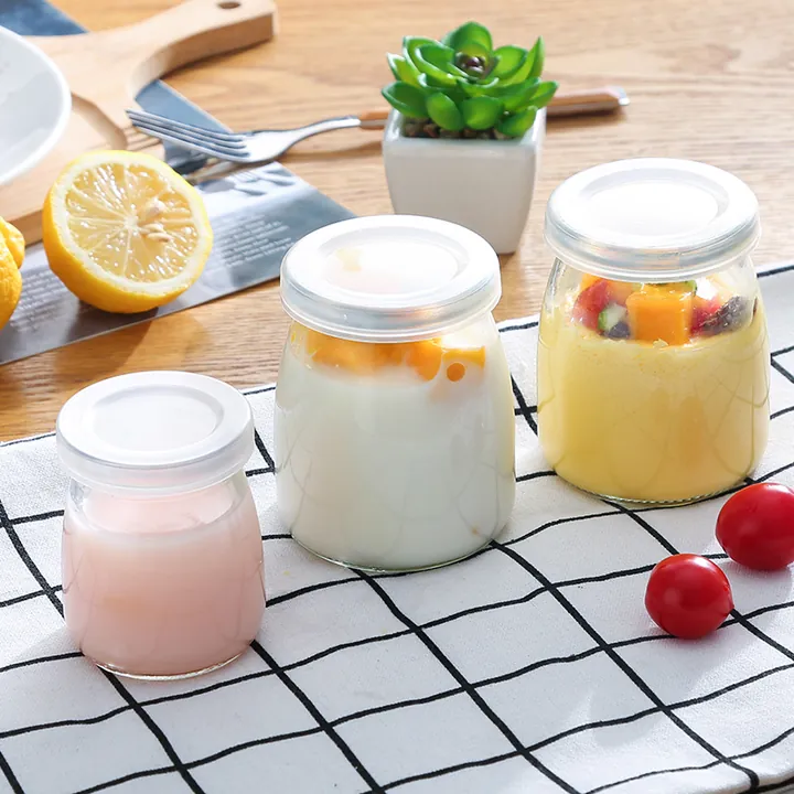Three yoghurt glass jars with white lids displayed with fruit on a table